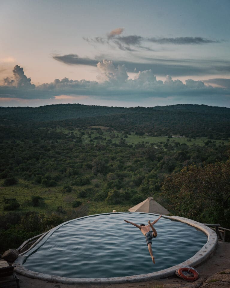 Man diving in infinity pool with savanna in back drop Mihingo Lodge Uganda