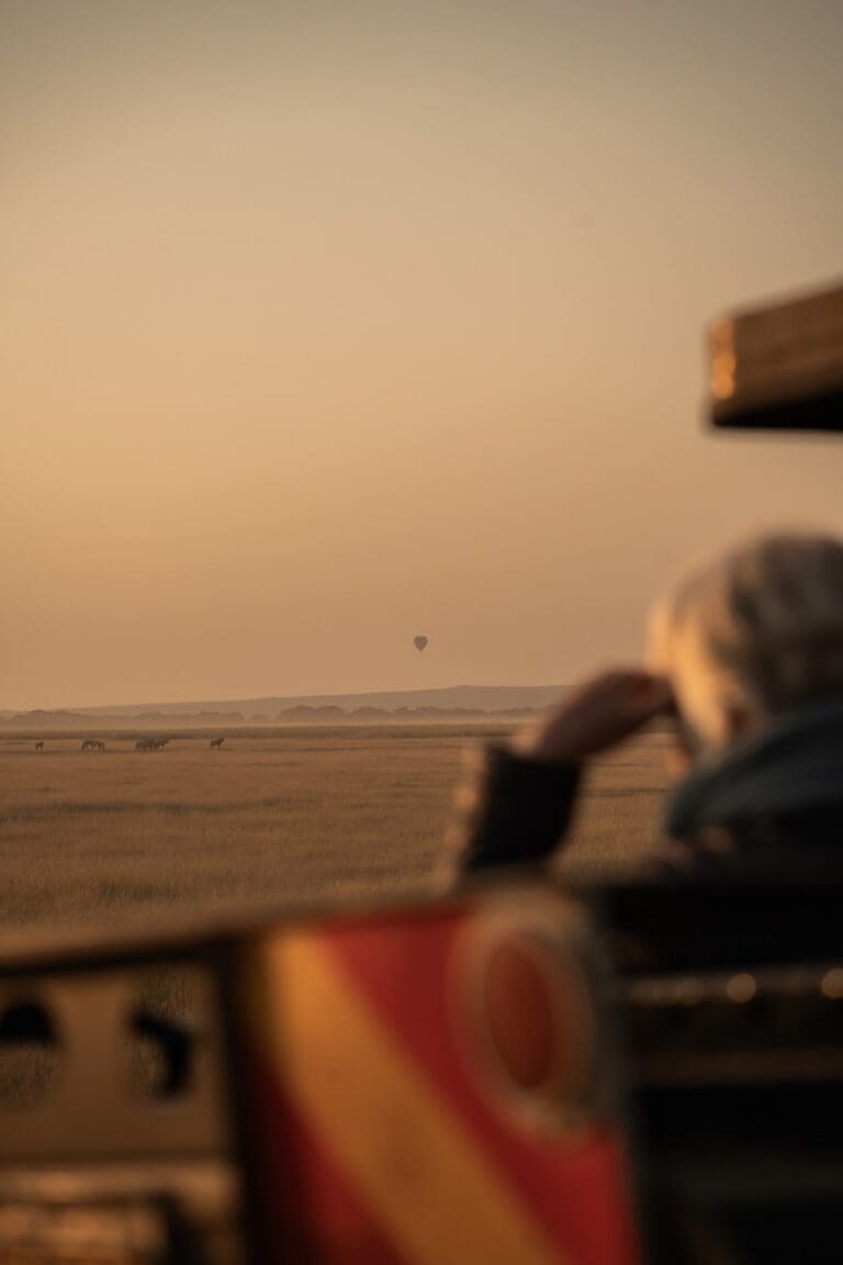 Person, die bei Sonnenaufgang auf Safari einen Heißluftballon und Zebras beobachtet