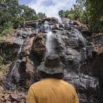 person in hat looking up at a large waterfall in Tanzania