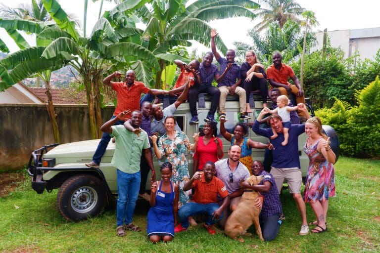 grote groep blije medewerkers en gasten die op en rond een safariwagen poseert