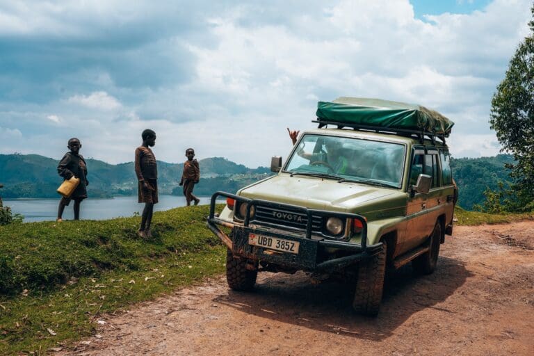 children watching a safari jeep by a lake in Uganda